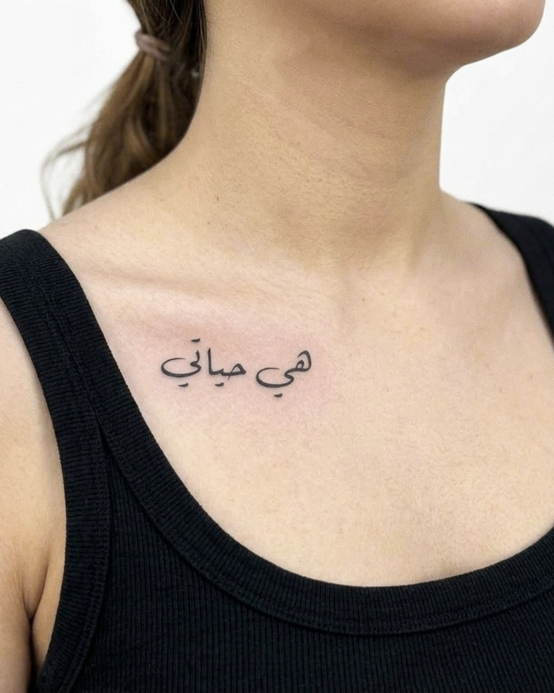 Person wearing a black tank top with a small My Love: Eternal Devotion — Semi-Permanent Tattoo on the neck